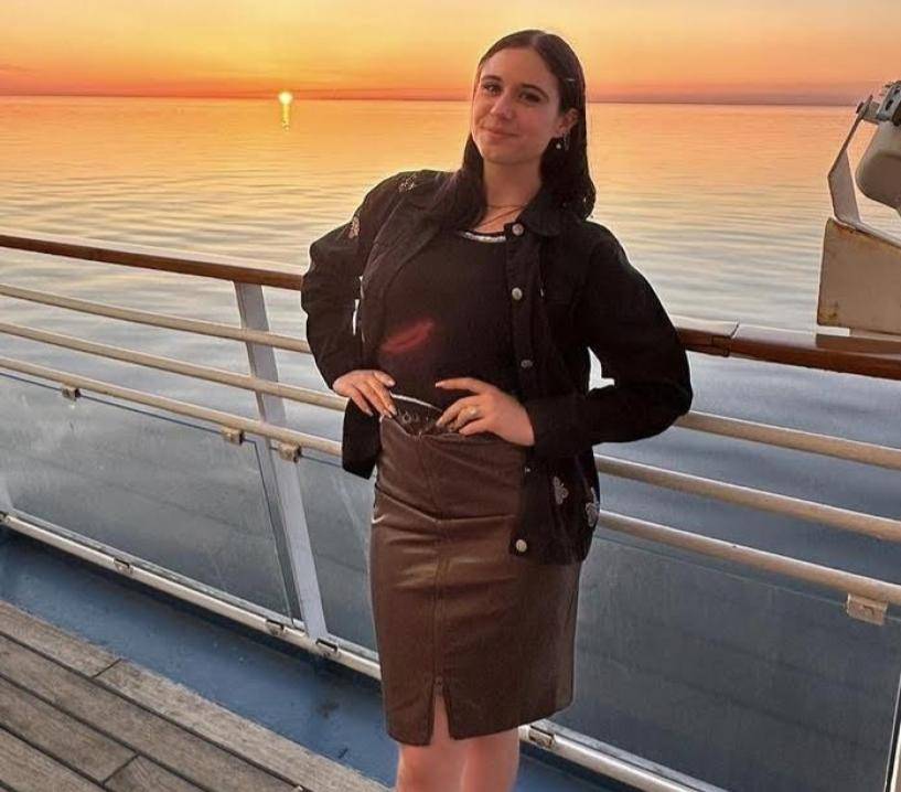 Smiling woman with hands on hips in front of sunset over a body of water